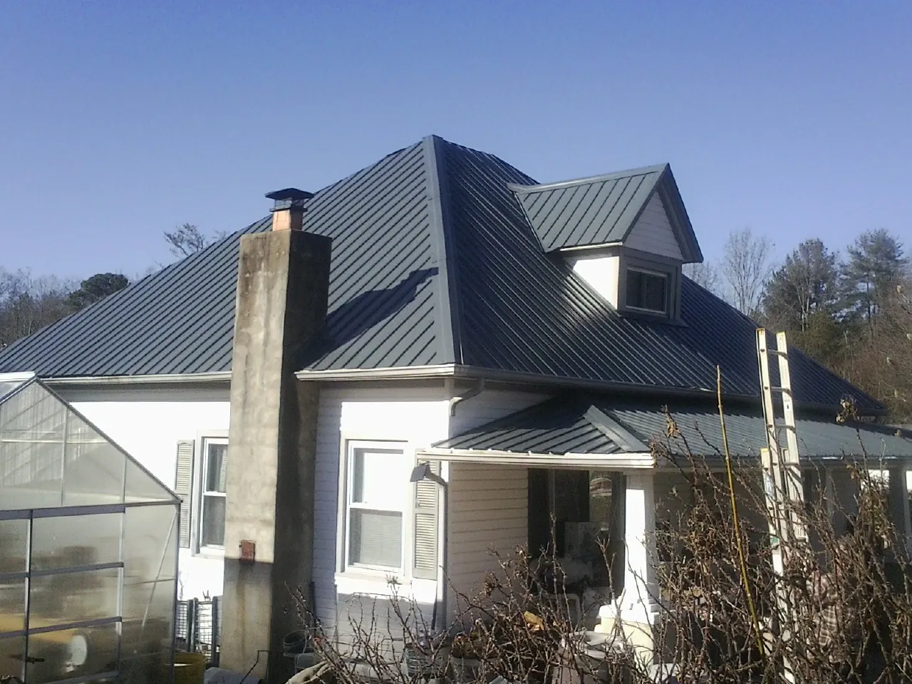 Dark blue standing seam metal roof on a white farmhouse with dormer in Sewaren