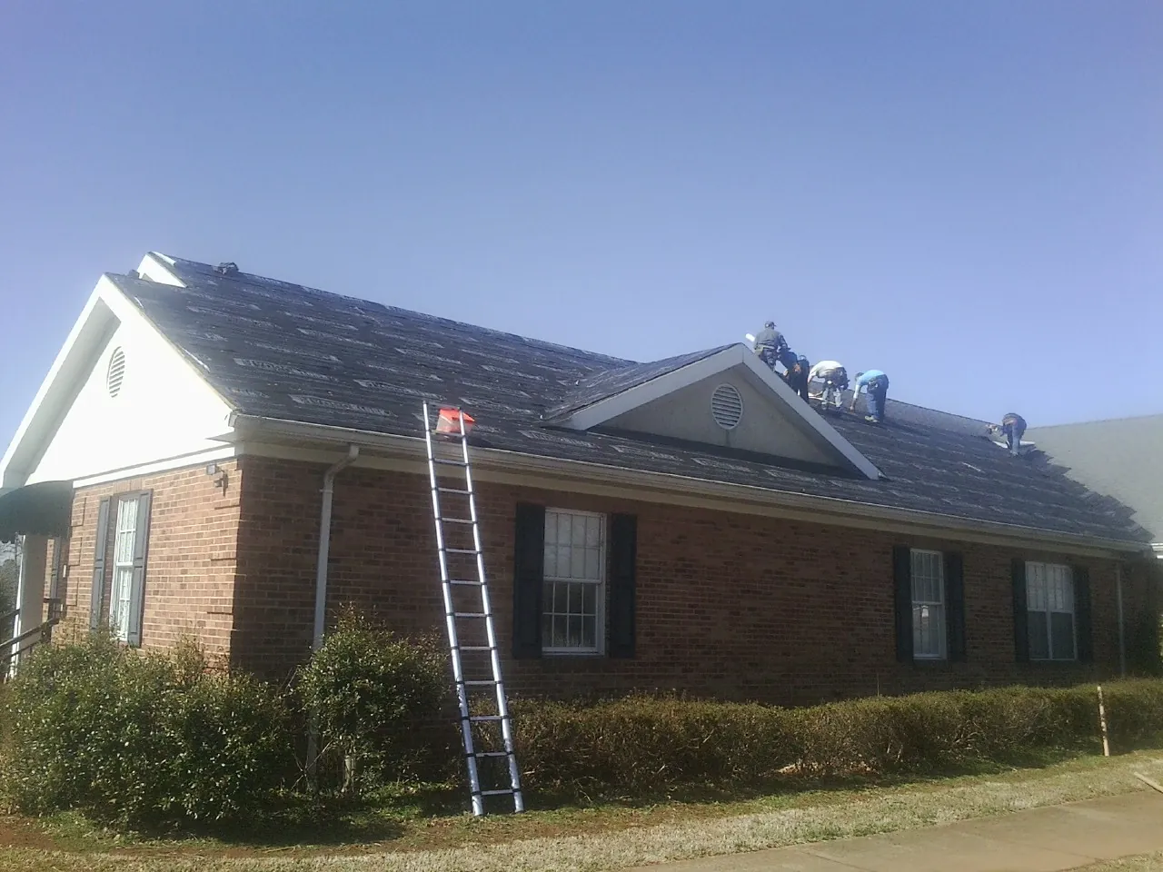 Crew tearing shingles off a brick ranch roof with a ladder set — Metal Roof Repair work by our crew in Sewaren