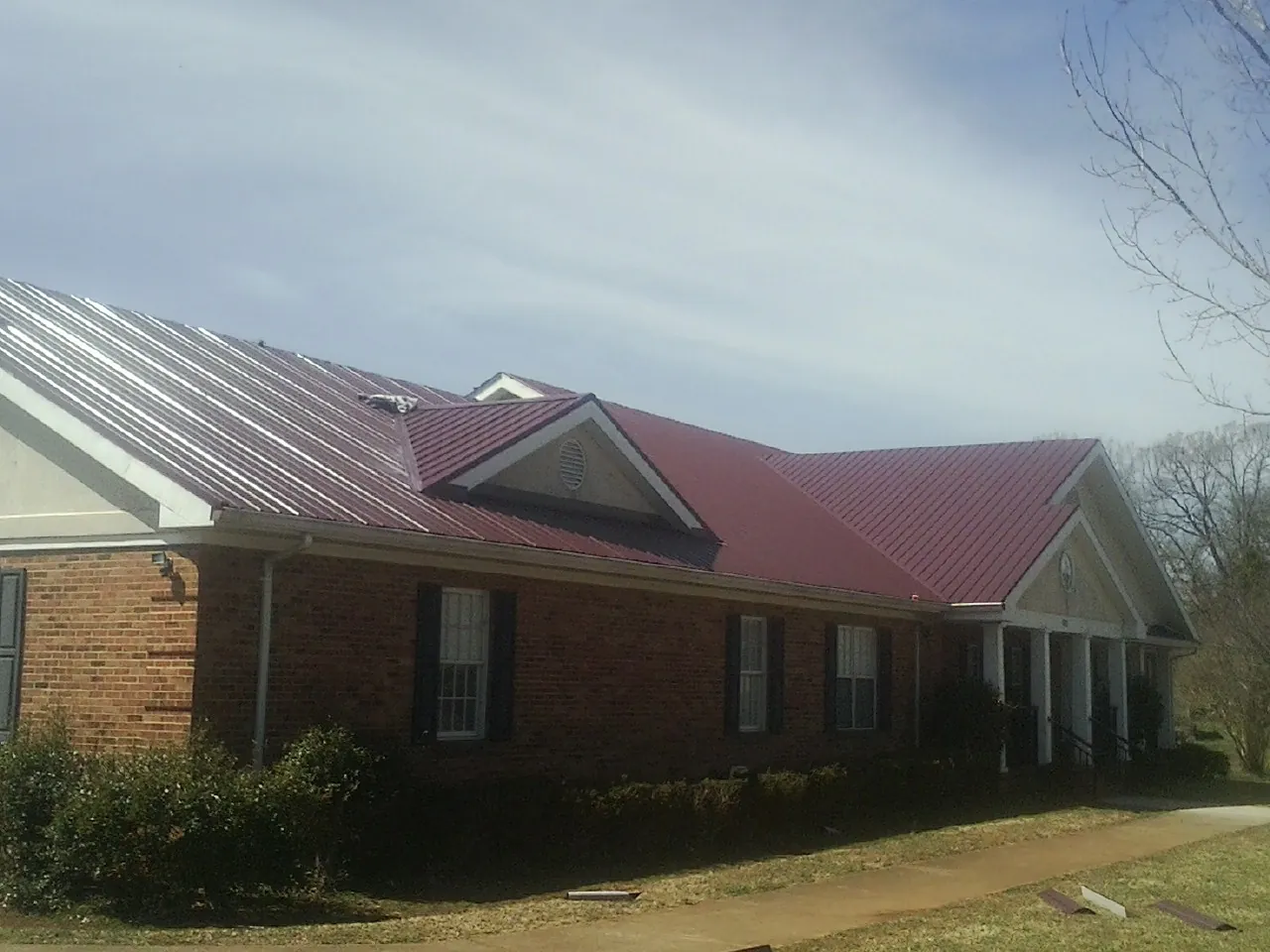 Red metal roof with gabled entries on a long brick building, from a Hail Damage Roof Repair job in Sewaren