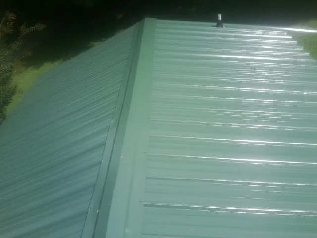 New green metal panels meeting at the ridge of a roof — Flat Roof Repair work by our crew in Sewaren