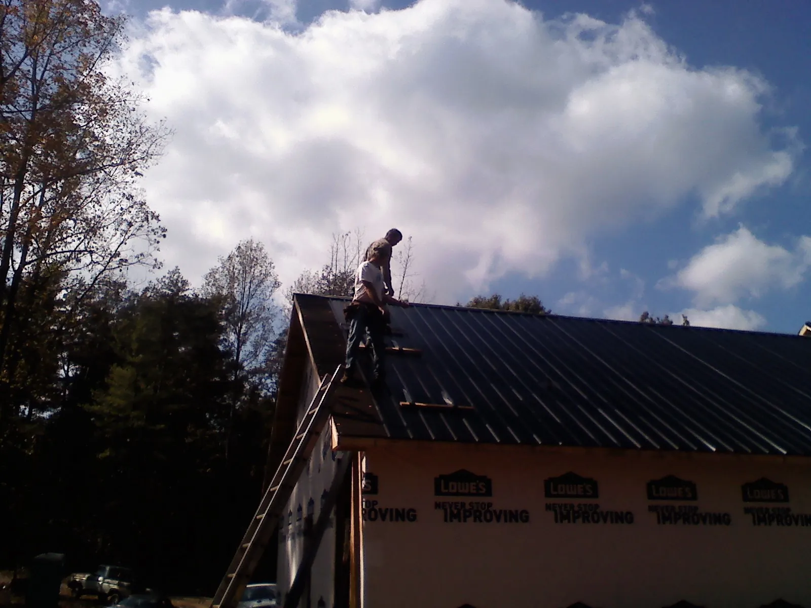 Roofer fastening dark metal panels high against a cloudy sky, from a Roof Inspection job in Sewaren